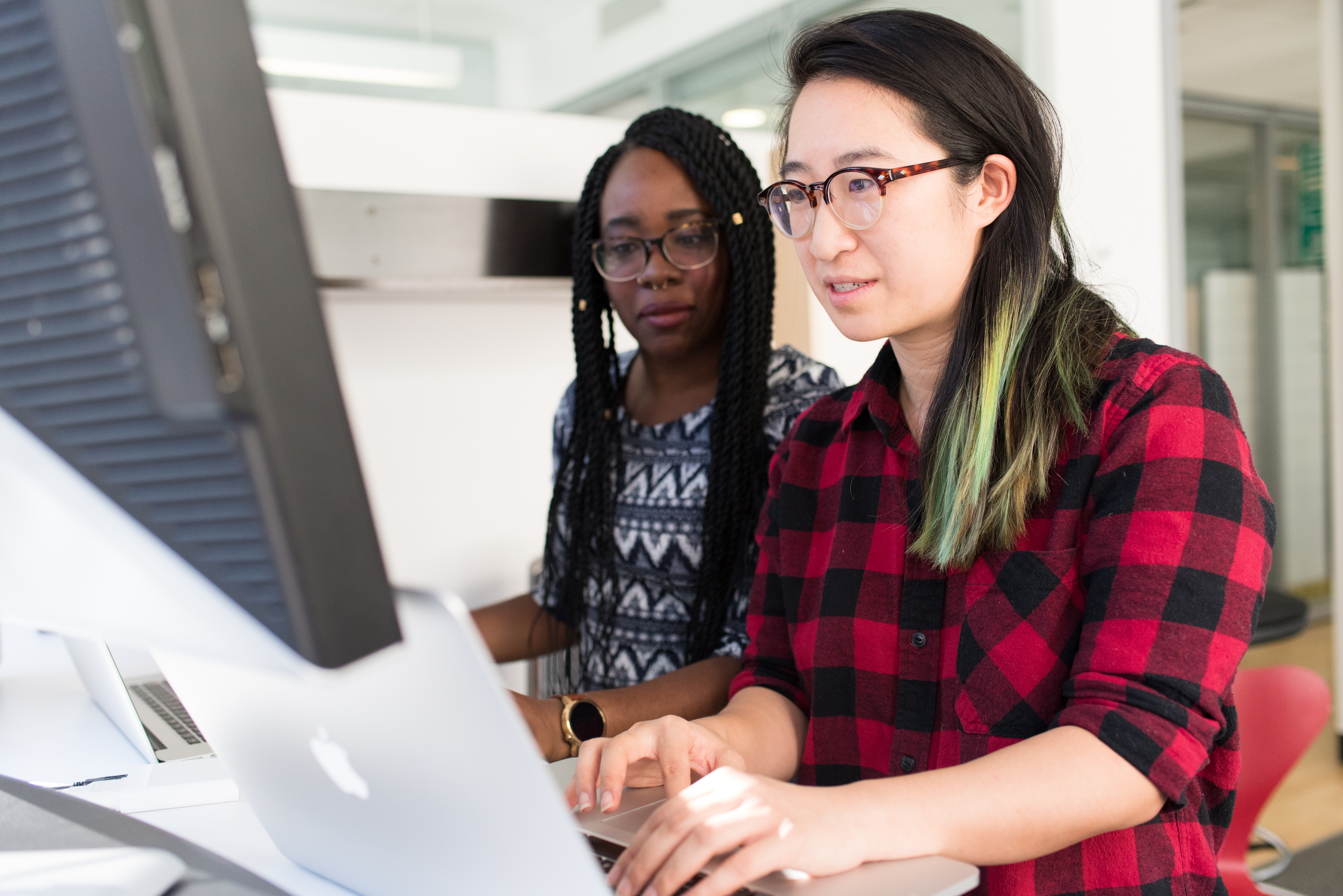 Two people collaborating on a silver macbook laptop